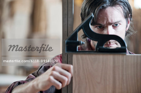 Caucasian man factory worker checking square measurements on a wooden part in a woodworking factory.