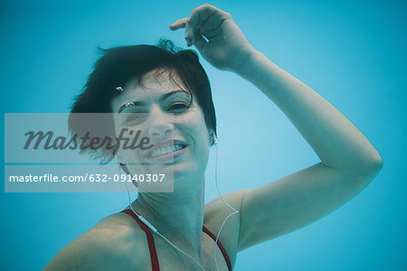 Woman listening to earphones underwater, smiling, portrait