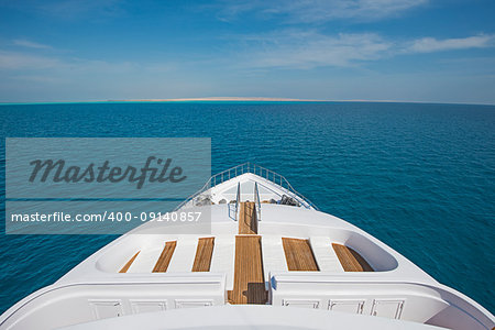 View over the bow of a large luxury motor yacht on tropical open ocean with sun beds