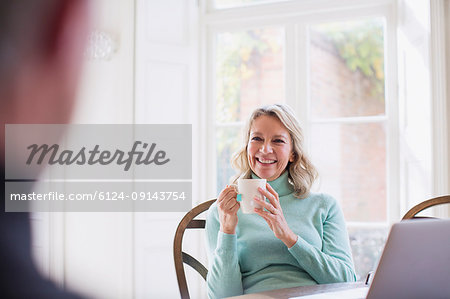 Smiling mature woman drinking tea, talking to man