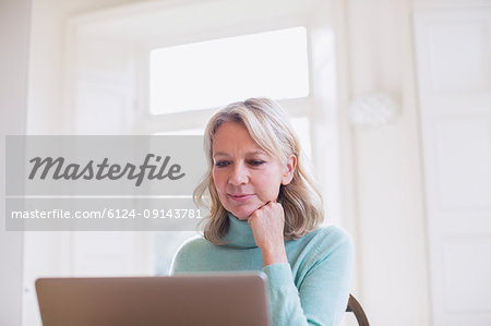 Focused mature female freelancer working at laptop at home