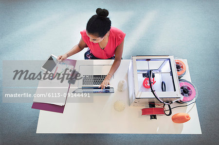 Female designer at laptop next to 3D printer