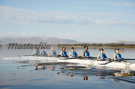 Female rowing team rowing scull on sunny lake Female rowing team rowing scull on sunny lake
