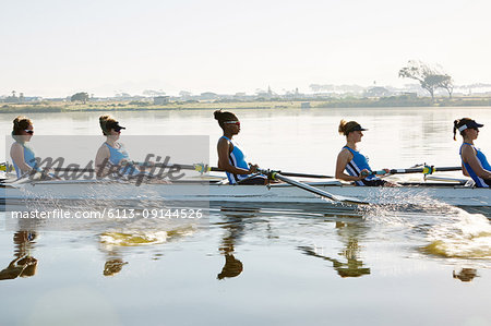 Female rowing team rowing scull on sunny lake