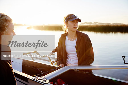 Focused female rower lifting scull at sunrise lakeside