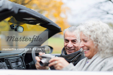 Senior couple using digital camera in convertible