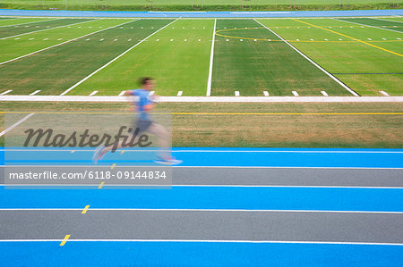 Side view of man running on blue track on sports field, motion blur.