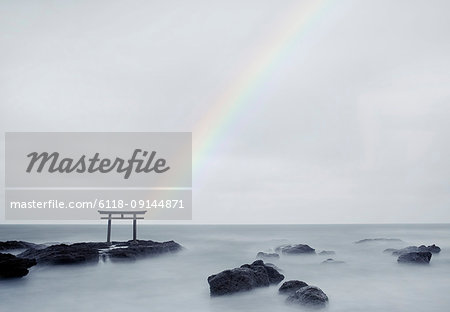 Rainbow over tall Torii gate on rocks in the middle of a lake.