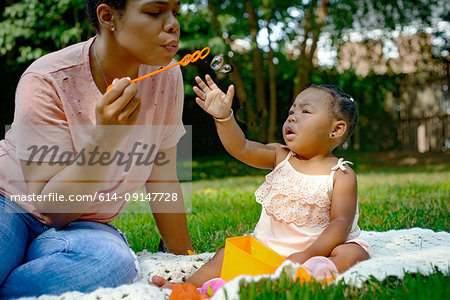 Mid adult woman blowing bubbles in garden for baby daughter