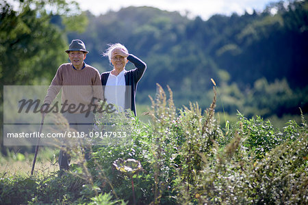 Husband and wife, elderly man wearing hat and using walking stick and elderly woman walking along path.