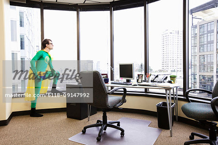 A Caucasian man office super hero stands at his office window pondering his next business move.