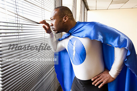 A black businessman office super hero looks out the window and checks his next business move.