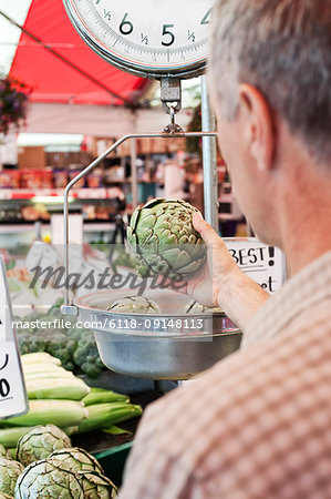 Over the shoulder view of man weighing artichoke at a fruit and vegetable market.