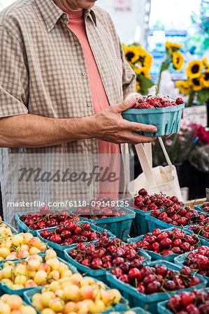 Man standing at stall, holding punnet with fresh cherries at a fruit and vegetable market.