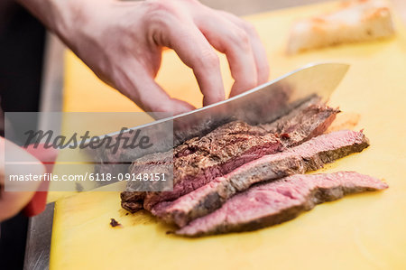 High angle close up of chef slicing beef with kitchen knife.