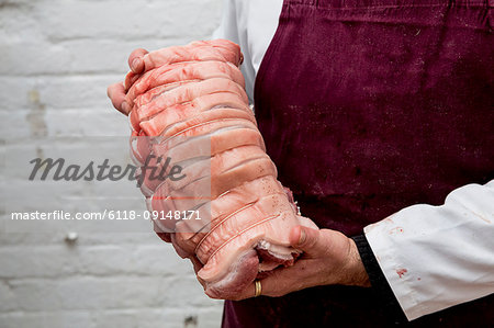 Close up of butcher wearing apron holding large rolled pork belly.