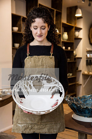 Woman with curly brown hair wearing apron holding a large intricate white ceramic bowl.