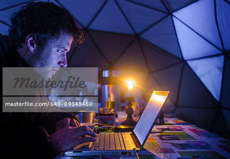 Man on expedition, using laptop in camp, Fletanes camp, Narsaq, Kitaa, Greenland