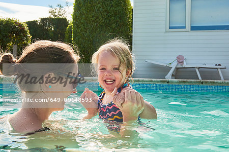 Woman holding toddler daughter hands in swimming pool