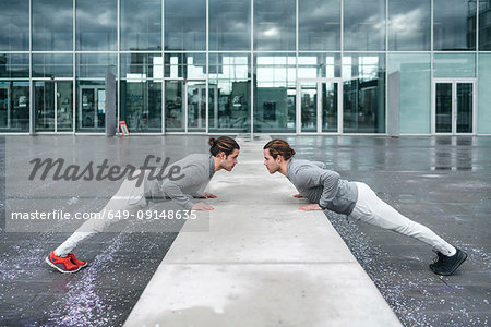 Young male twins doing push ups against wall in city, full length