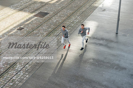 Young adult male twins running together, running along sidewalk, high angle view