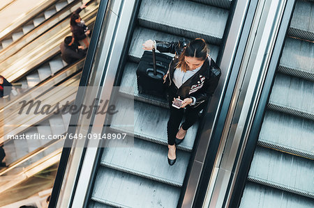 Woman on escalator, holding suitcase, overhead view