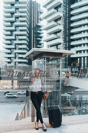 Businesswoman, outdoors, holding wheeled suitcase, using smartphone