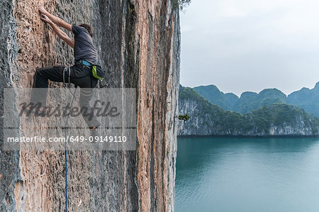 Man rock climbing on limestone rock, Ha Long Bay, Vietnam