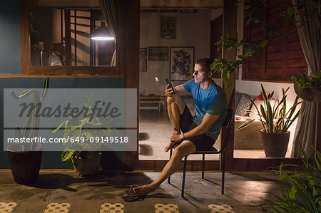 Mature man sitting on patio at night looking at smartphone