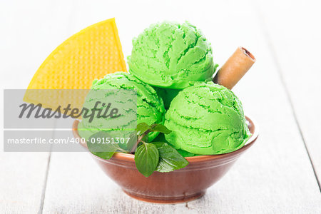 Scoop of pistachio ice cream in bowl on wooden background.