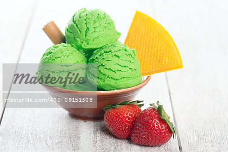 Scoop of honeydew ice cream in bowl on wooden background.