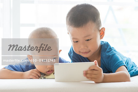 Young children addicted to technology gadget. Asian boys playing with smart phone at home.