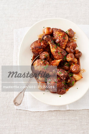 Chicken with wine sauce (Coq Au Vin) on a white platter with serving spoon