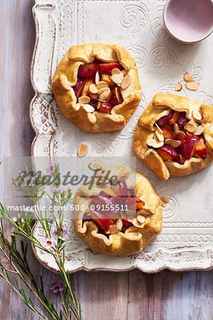 Three plum almond galettes on a decorative, rustic serving tray with purple flowers