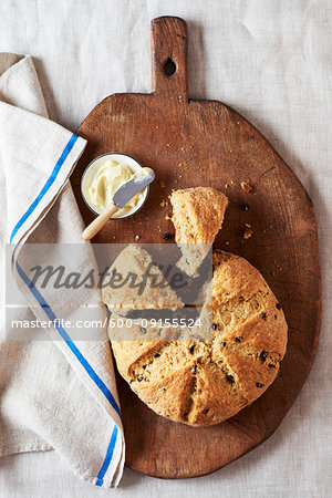 Irish soda bread with currants and a small dish of butter on a wooden cutting board