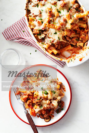 Baked ziti with mushrooms in a casserole dish with a portion on a plate with a fork in front