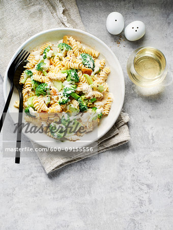 Rotini with broccoli in a cream sauce and a glass of white wine on a grey background
