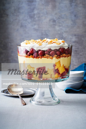 Cherry trifle in a glass trifle bowl with serving spoon on grey background