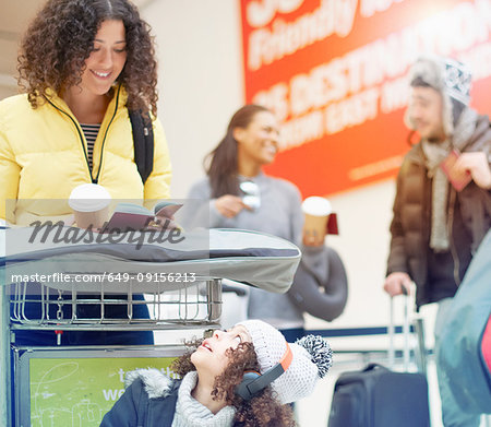 Girl looking up at mother looking at passport on luggage trolley in airport departure lounge