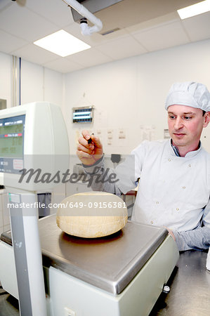 Cheese maker weighing wheels of hard cheese