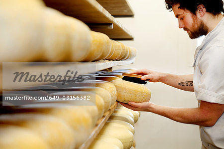 Cheese maker brushing mould off the hard cheeses by hand