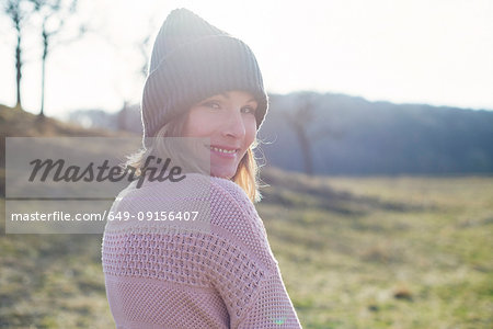 Sunlit portrait of mid adult woman in sunlit field looking over her shoulder