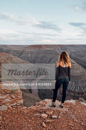 Young woman in remote setting, standing on cliff edge, looking at view, rear view, Mexican Hat, Utah, USA