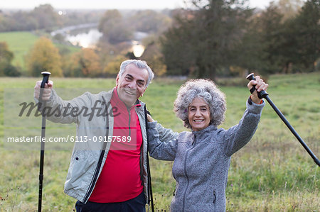 Portrait enthusiastic, confident active senior couple hiking with poles in rural field