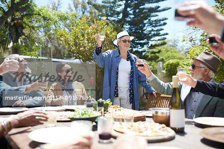 Happy senior woman toasting wine with friends at sunny garden party