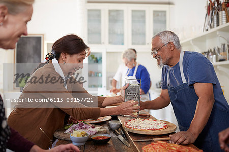 Senior couple shredding cheese over fresh pizza in cooking class