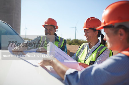 Engineers reviewing blueprints on truck at sunny wind turbine power plant