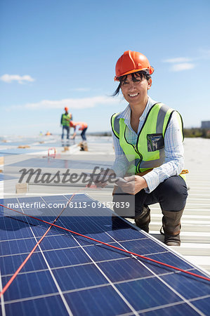 Portrait confident, smiling female engineer with digital tablet examining solar panels at power plant