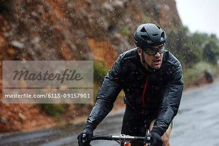 Dedicated young man cycling on rainy road