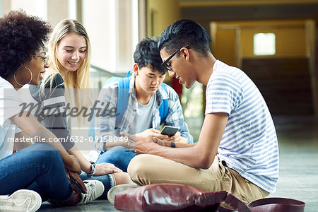 Friends sitting together on floor of school corridor between classes